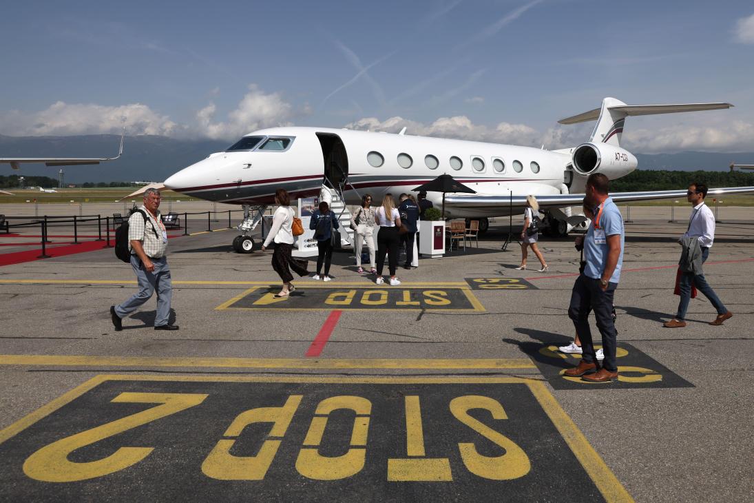 White private jet parked on tarmac with passengers boarding and ground crew nearby