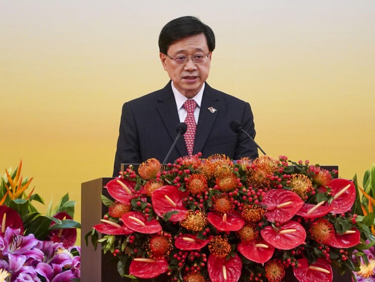 Hong Kong Chief Executive John Lee speaking at a podium with elaborate floral arrangements