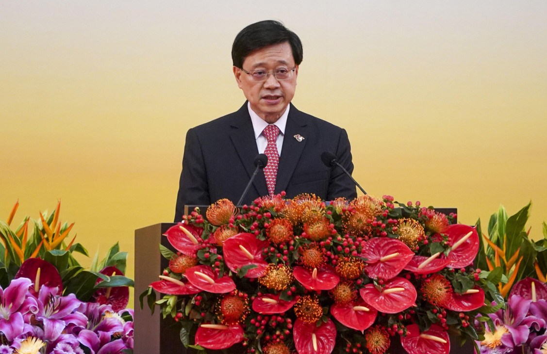 Hong Kong Chief Executive John Lee speaking at a podium with elaborate floral arrangements