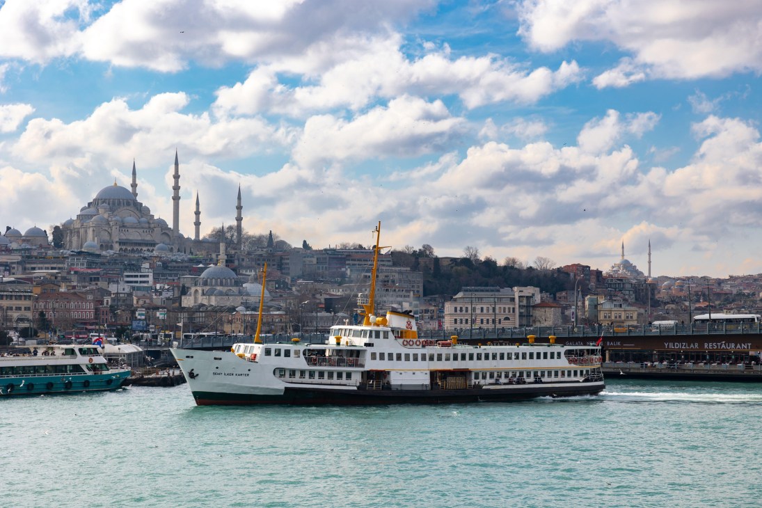 Ferry boat crossing water with Istanbul skyline featuring mosque with minarets and historic buildings in background