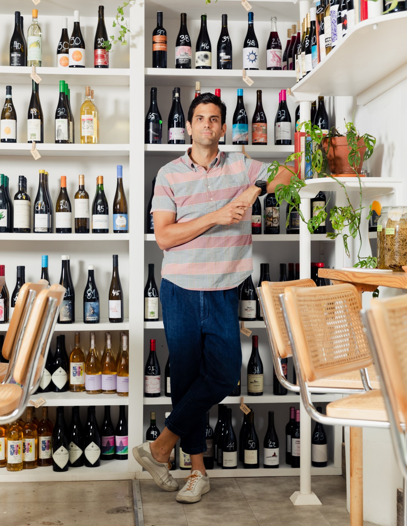 Josh Hackler stands in his restaurant surrounded by shelves of wine bottles, holding a bottle