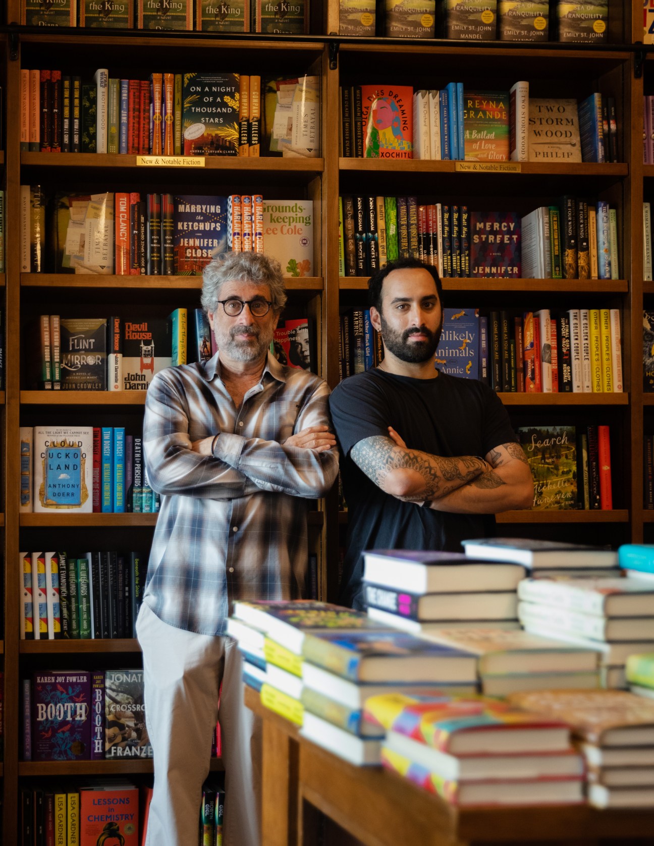 Two men with crossed arms standing in front of floor-to-ceiling bookshelves in a bookstore