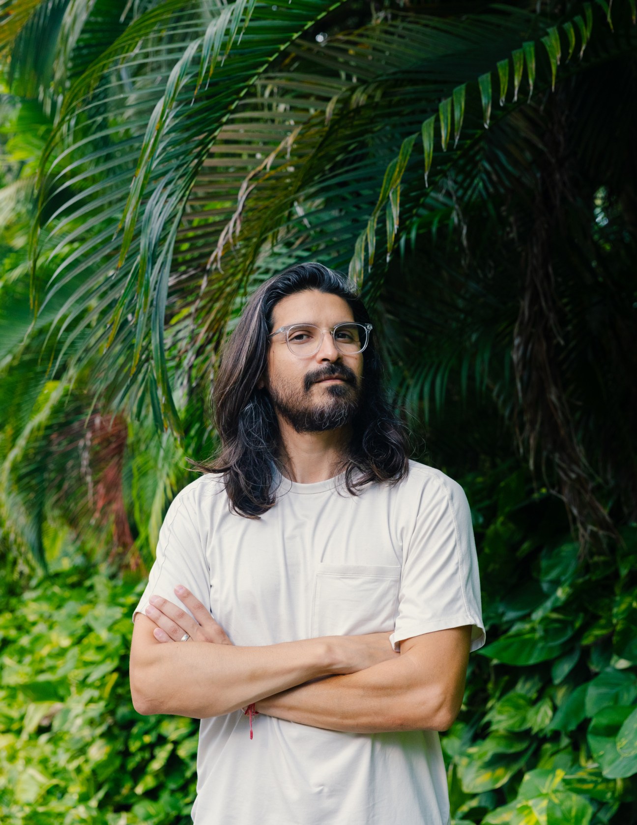 Pablo Quiroga standing with arms crossed outdoors surrounded by tropical palm plants
