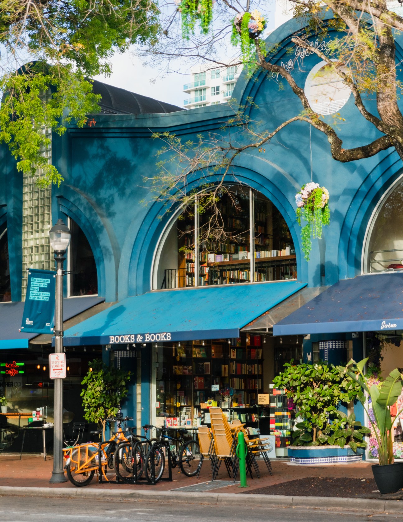 Books & Books storefront with distinctive blue curved architecture, outdoor seating, and bicycles parked in front