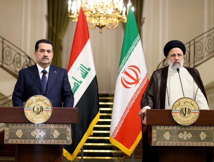 Two officials at podiums with Iraqi and Iranian flags during diplomatic meeting