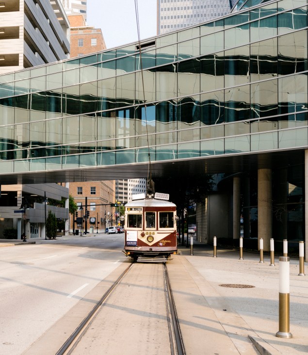 Historic trolley car traveling on tracks through downtown Dallas with modern glass buildings overhead