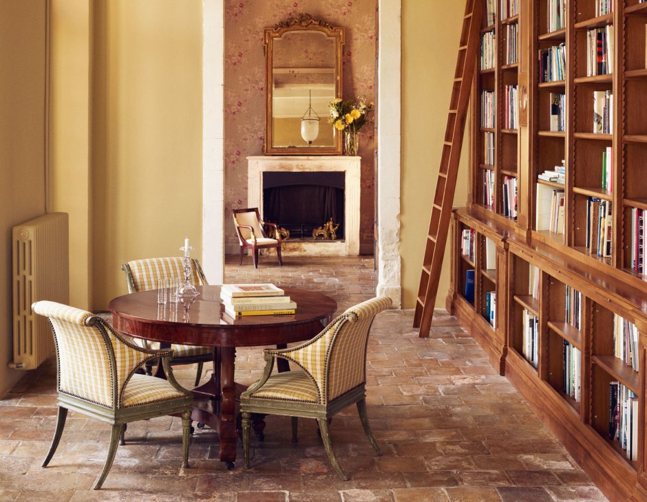 Library interior with floor-to-ceiling bookshelves, ladder, round table with striped chairs and fireplace