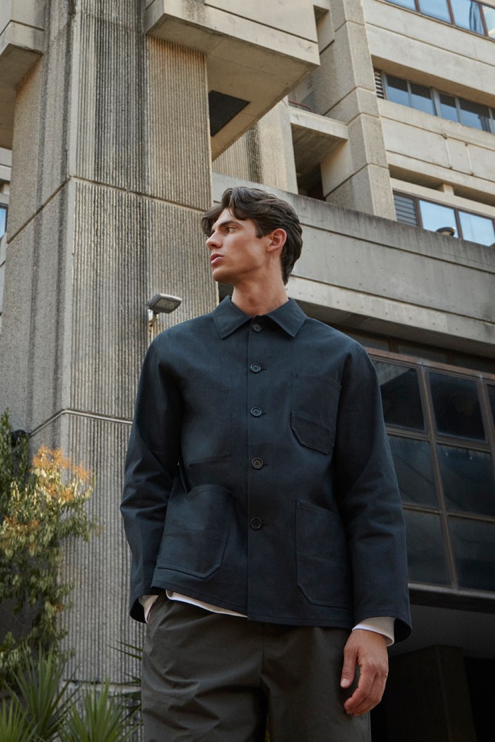Man in dark navy button-up jacket looking upward against concrete building background