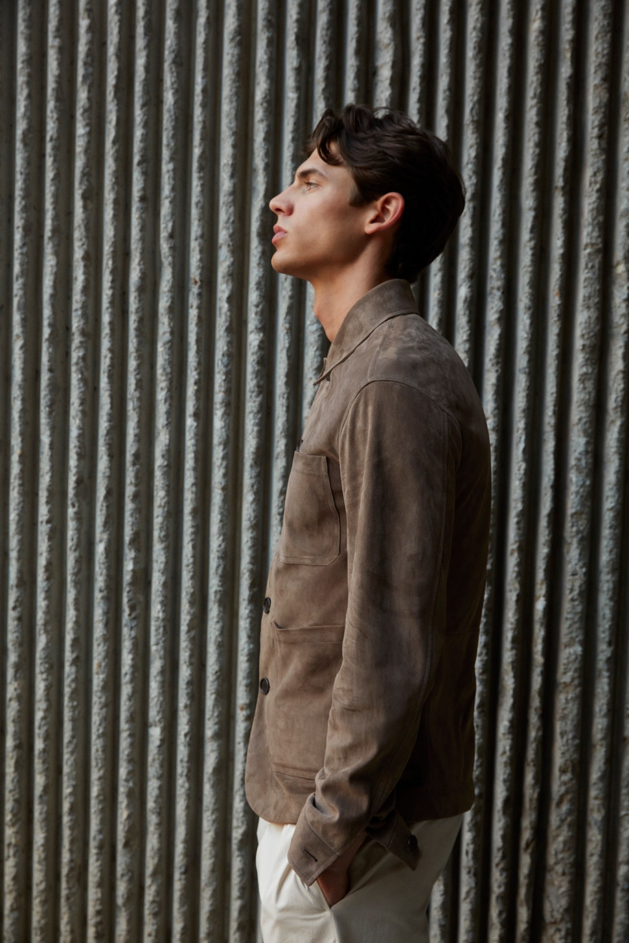 Man in profile wearing brown suede jacket against textured concrete wall background