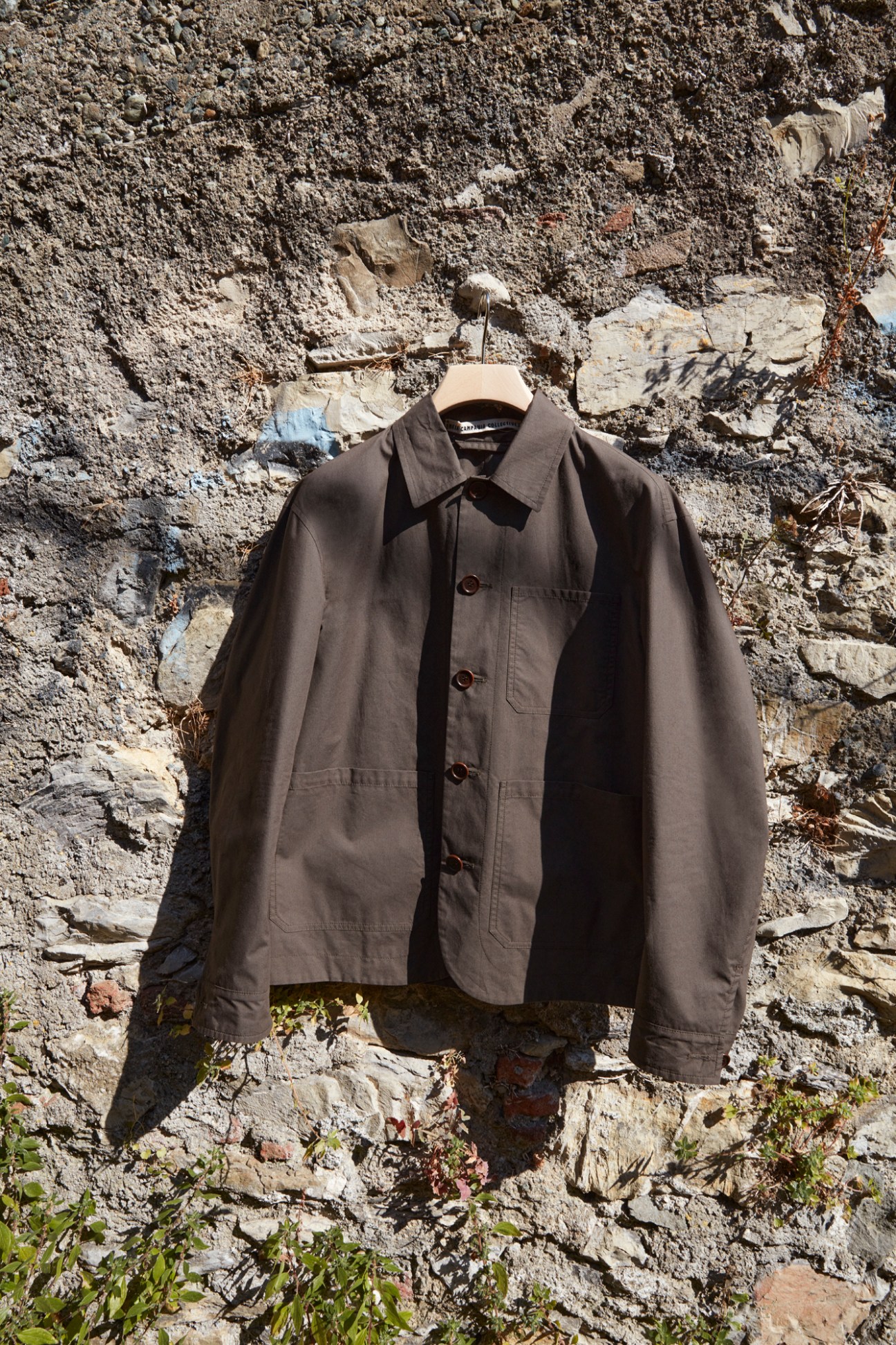 Brown hemp wool jacket with collar and button front hanging on hanger against stone wall background