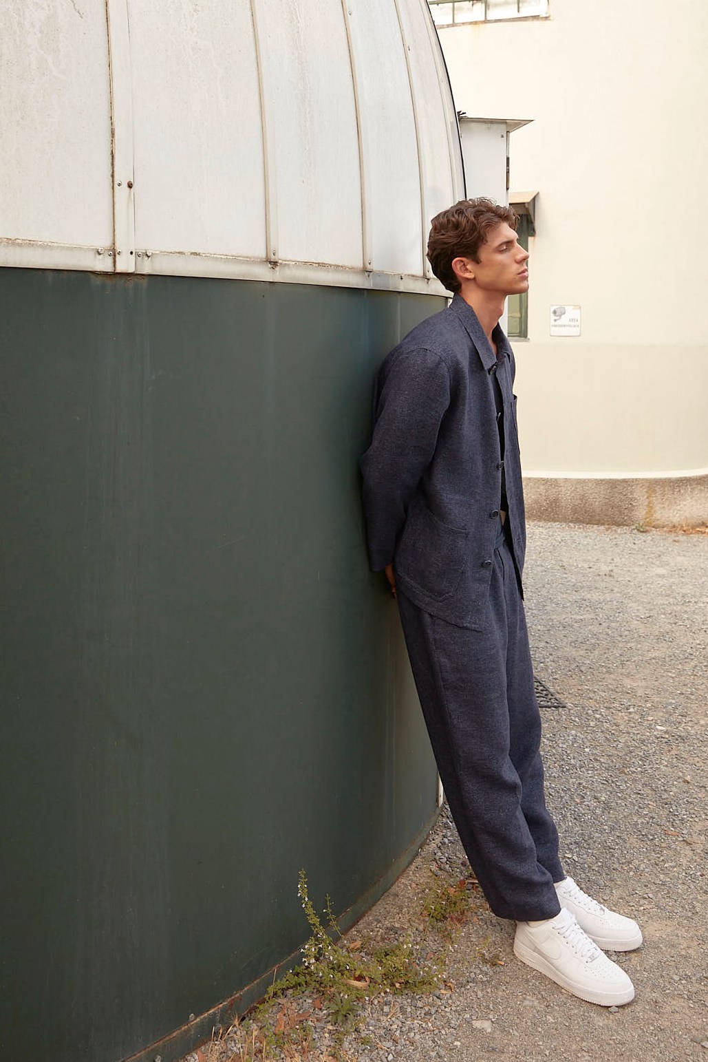 Man in navy blue jumpsuit leaning against green wall in urban setting