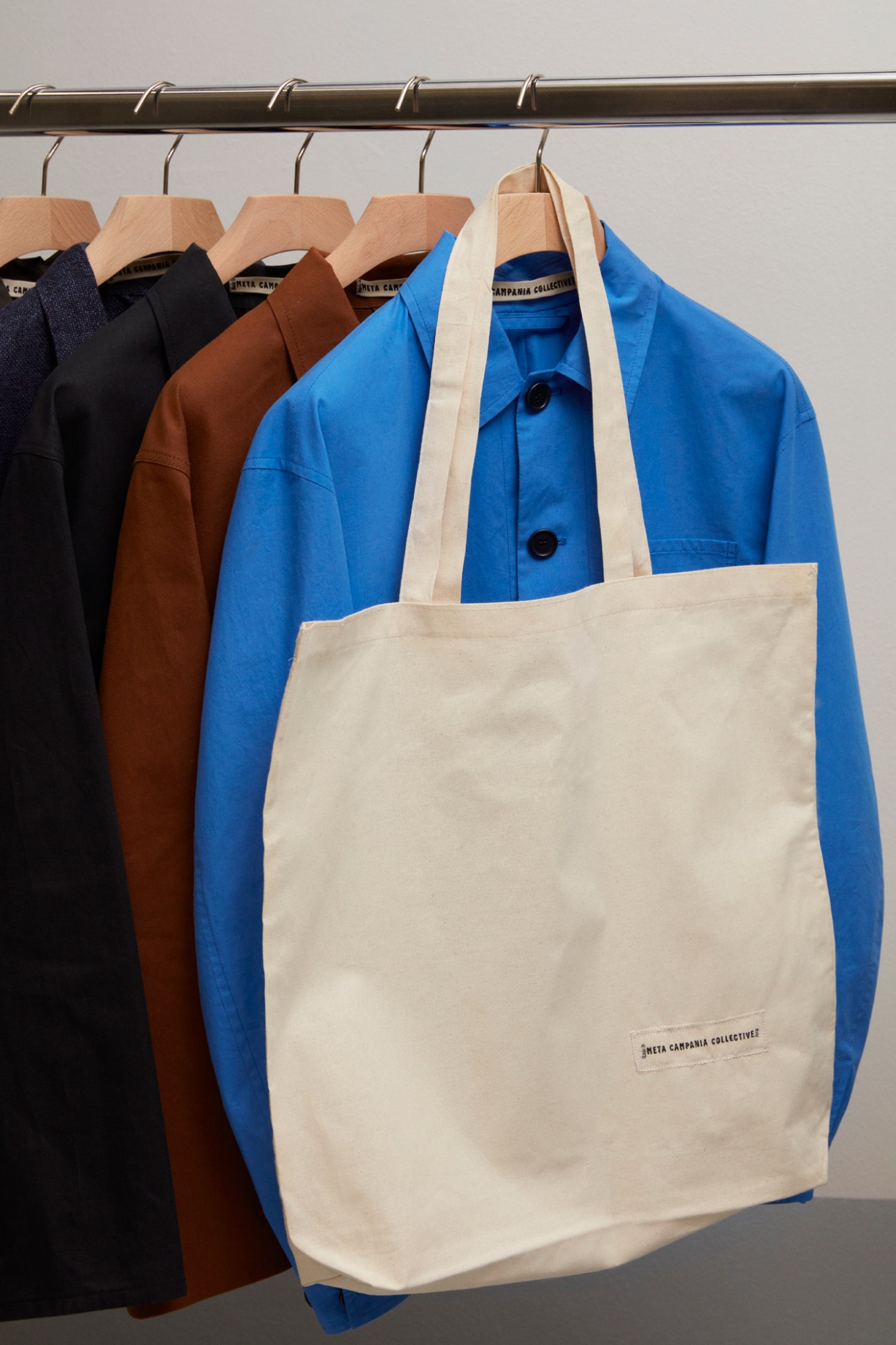 Clothing rack with jackets in navy, brown and blue colors hanging on wooden hangers with cream canvas tote bag