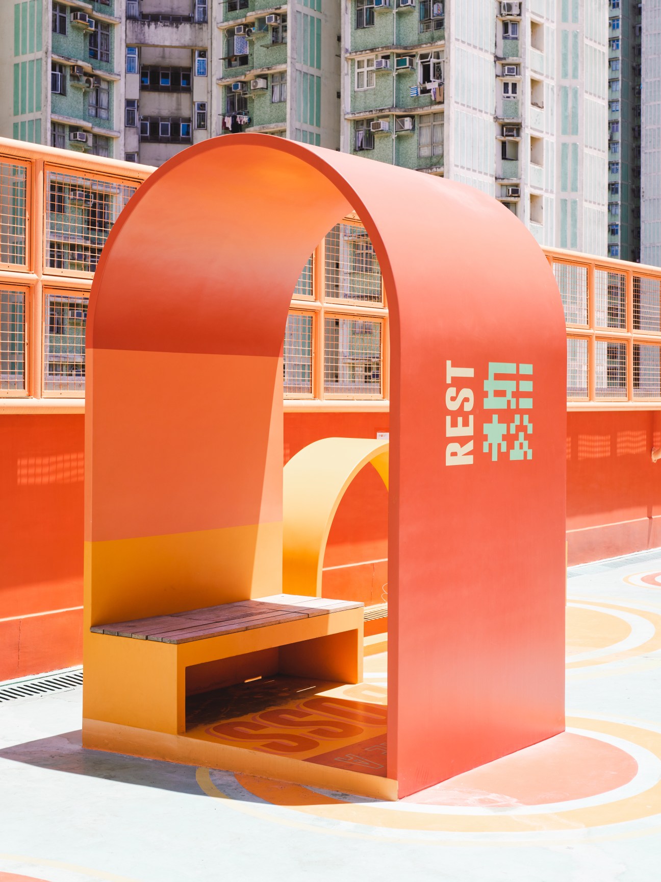 Orange curved shelter with bench and REST text at Ming Tak sports court