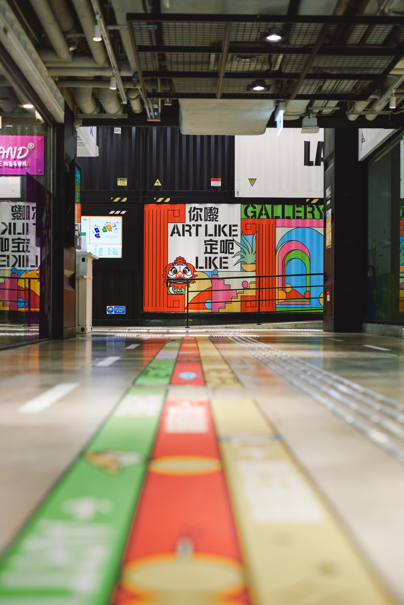 Colorful art mural at Lai Kok shopping centre entrance in Hong Kong, featuring a red-framed design with playful characters and geometric shapes, with rainbow artwork visible on the right side