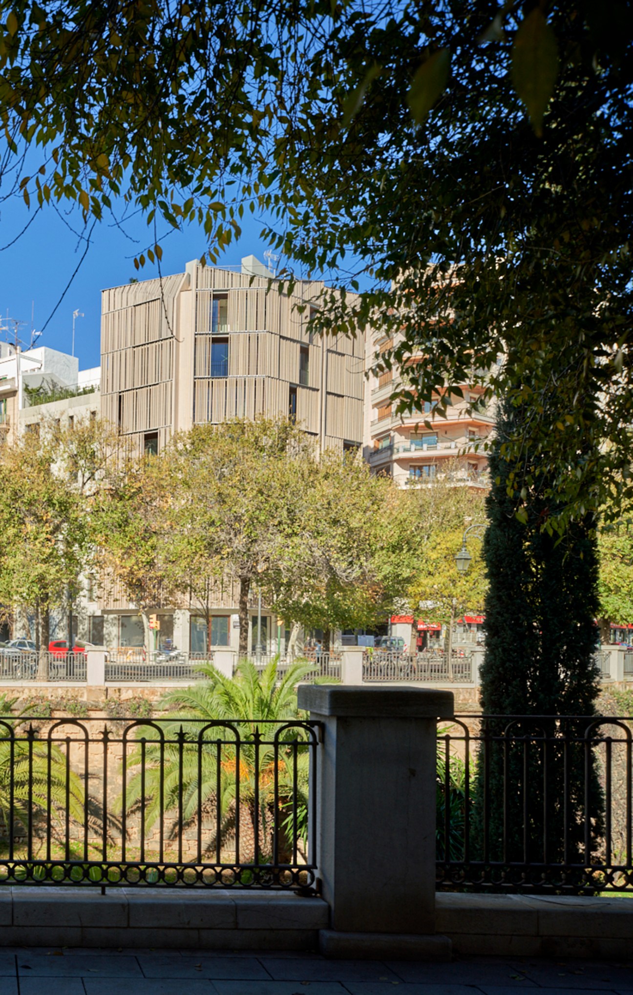 Modern building with vertical timber facade viewed through tree branches and metal railing