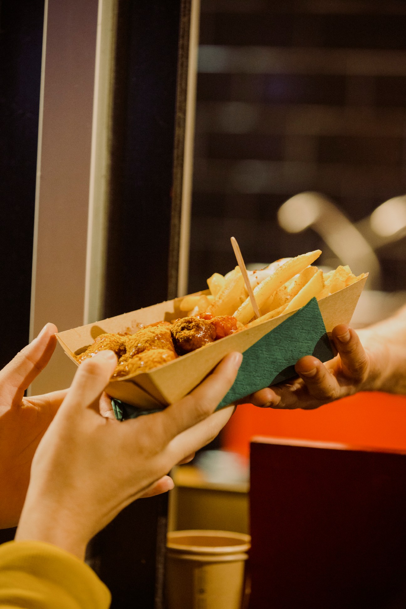 Hands holding paper container of currywurst with fries and curry sauce being prepared fresh