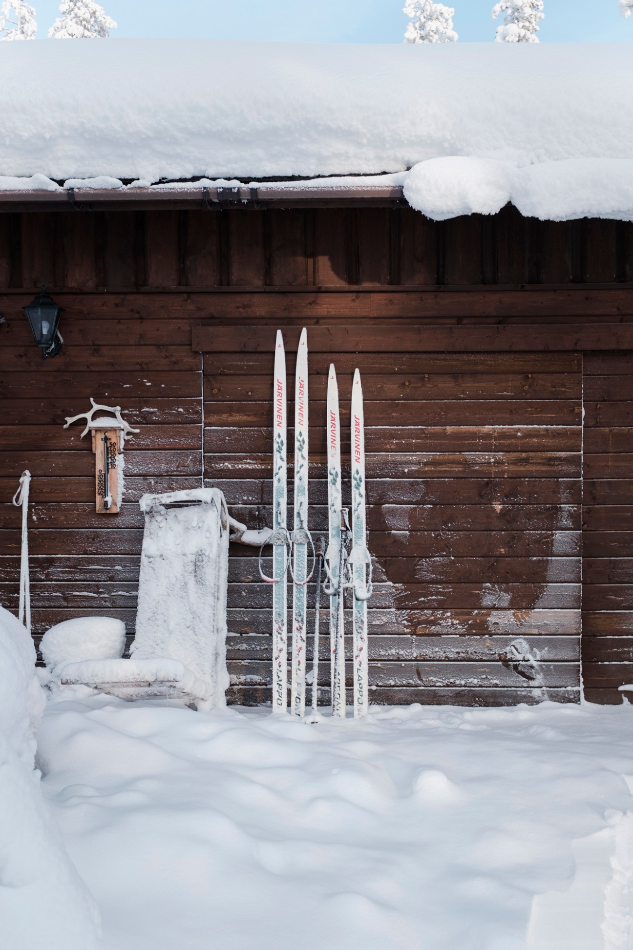 Cross-country skis leaning against a snow-covered wooden cabin wall in winter