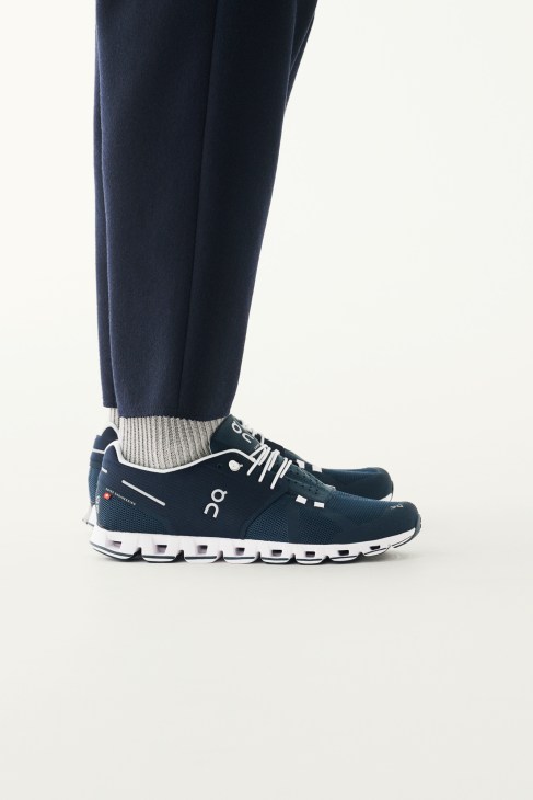 Navy trousers, ribbed socks and black and white On trainers styled on a model's lower legs.