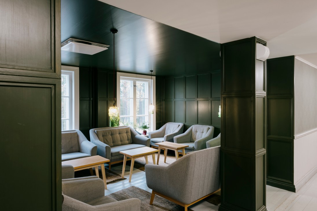 Dark green paneled walls frame a lounge area with grey upholstered armchairs and wooden side tables at Hotelli Punkaharju.