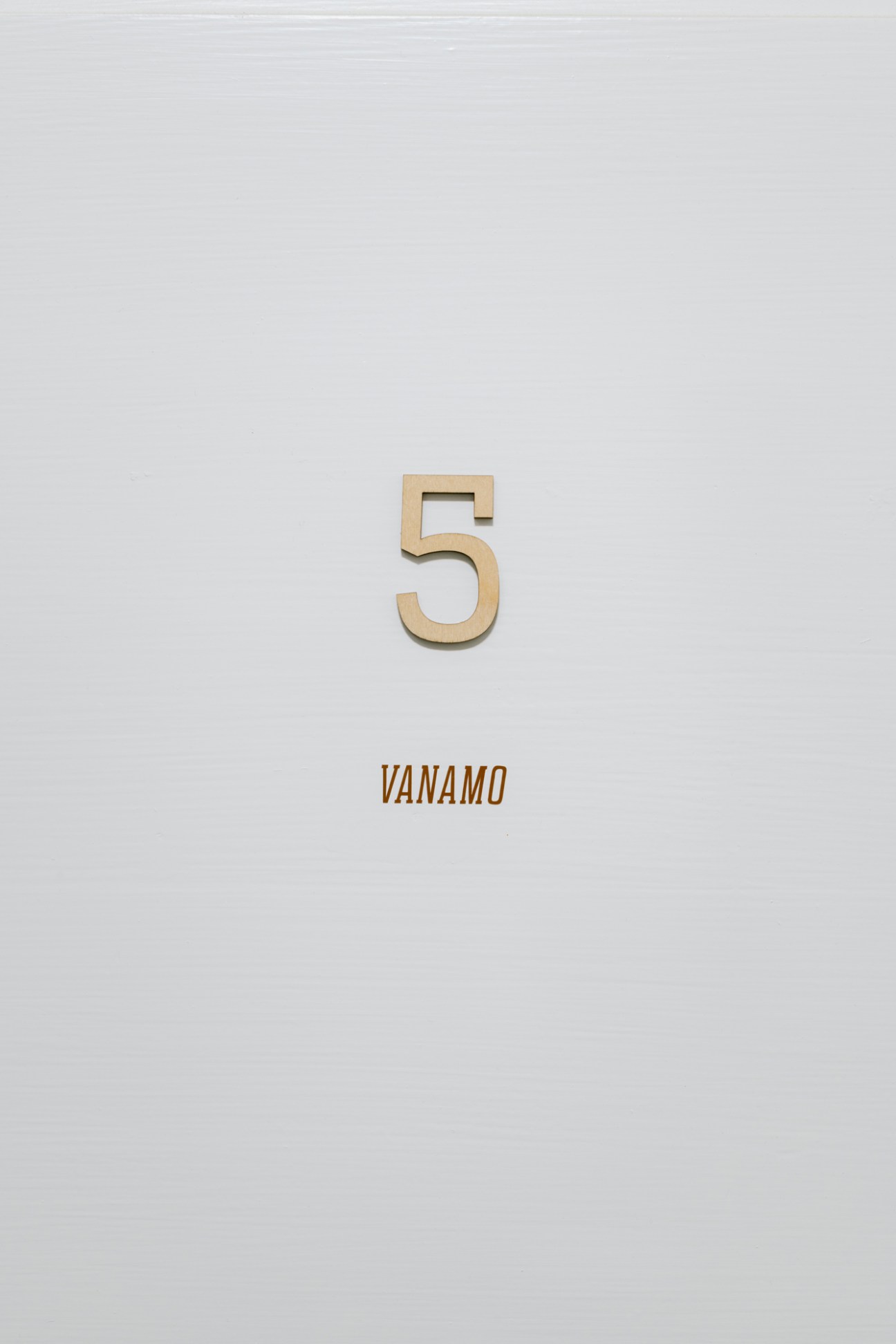 A wooden number 5 mounted on a white wall with 'VANAMO' text below it.