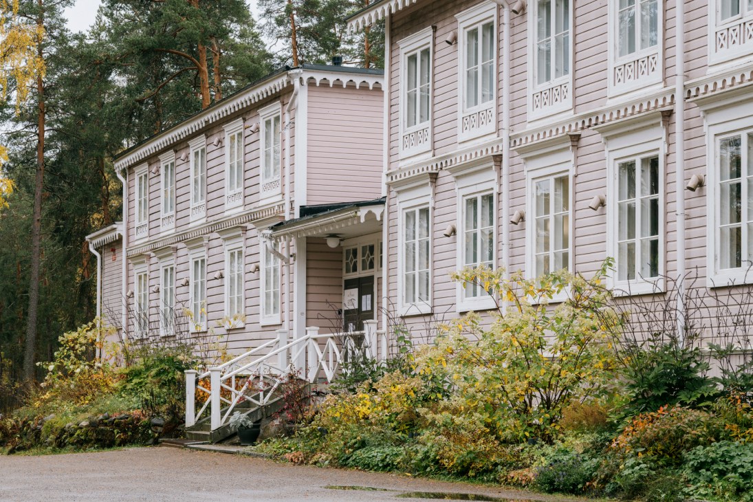 Pink-painted wooden farmhouse exterior with white trim windows and decorative railings surrounded by overgrown garden vegetation.