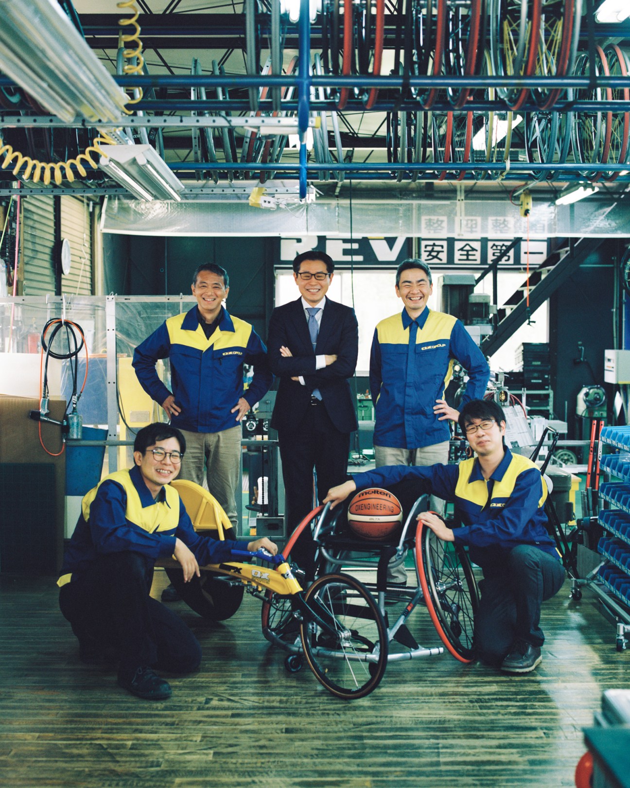 OX Engineering president Katsuyuki Ishii with team members in their workshop, surrounded by high-performance sports wheelchairs