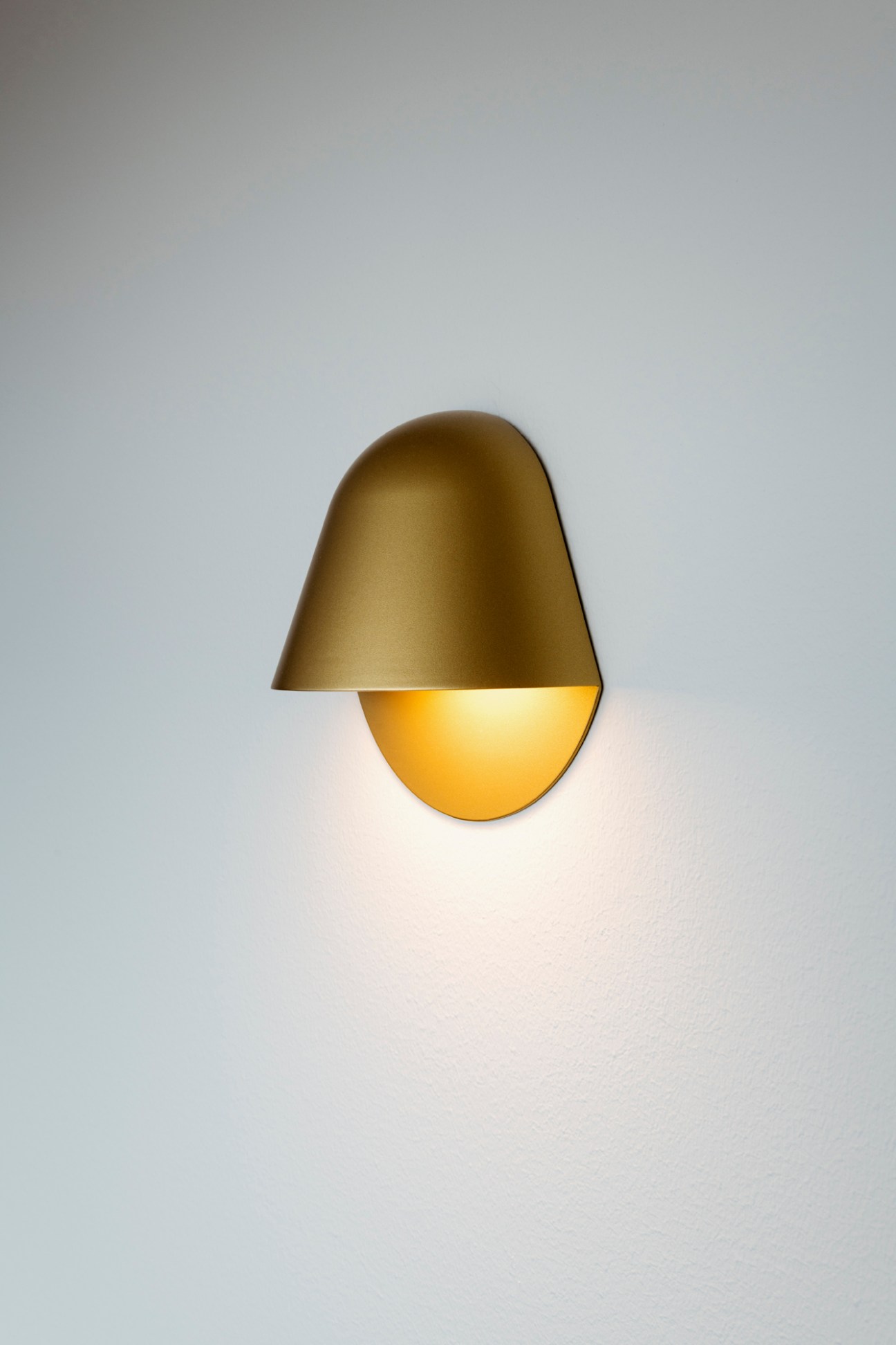 Modern brass wall sconce with warm lighting mounted on white wall