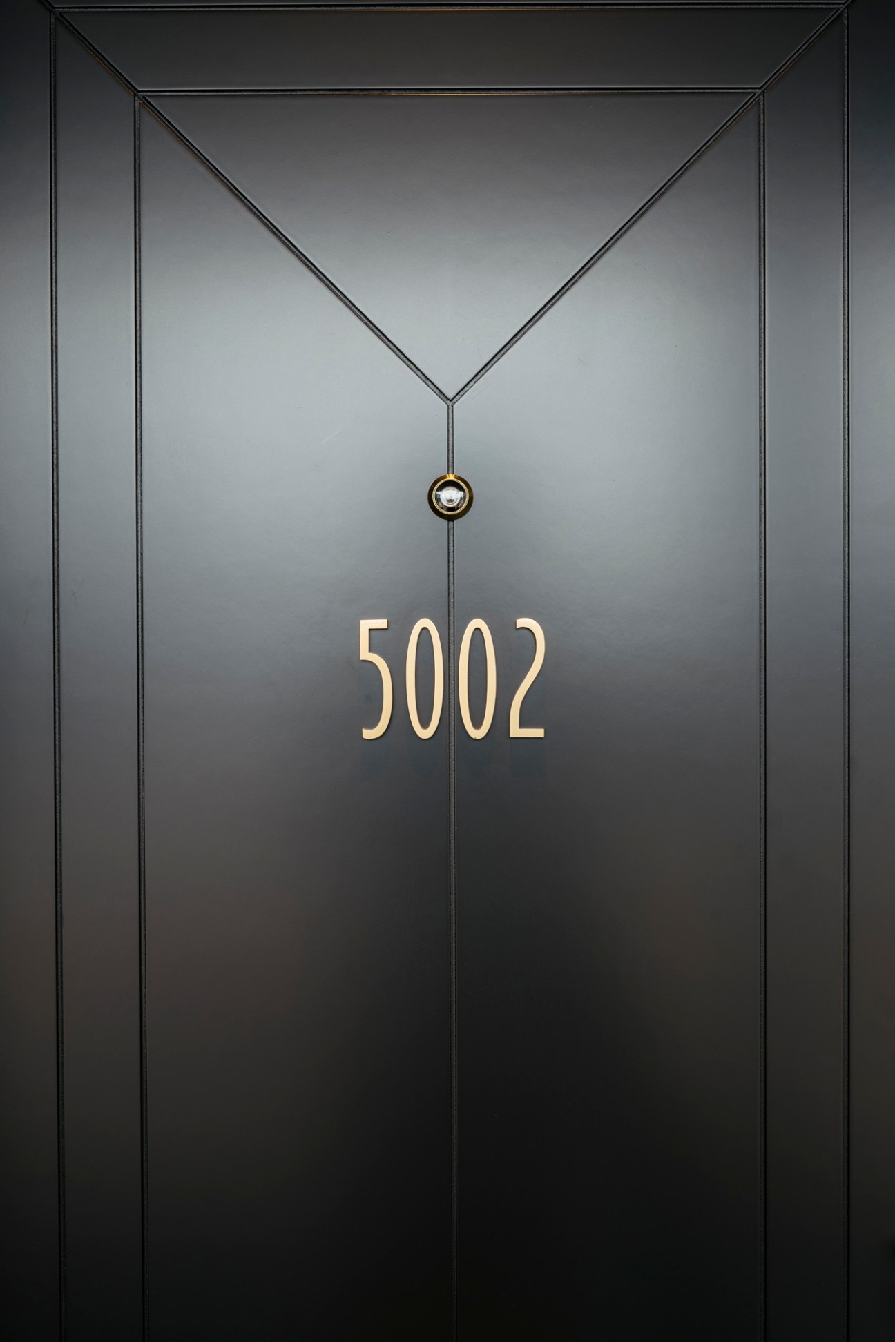 Dark hotel room door with gold number 5002 and modern geometric paneling design
