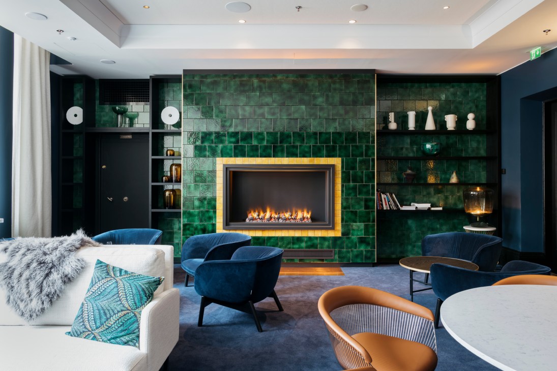 Elegant hotel lounge with emerald green tiled fireplace, navy blue velvet chairs, and built-in shelving