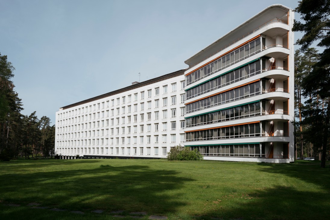 Paimio Sanatorium's white modernist patients' wing with orange and green accents surrounded by pine forest.