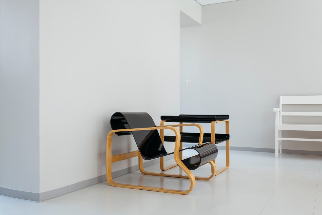 Alvar Aalto's Paimio chair with black seat and curved wooden frame next to matching tray table in white minimalist interior.