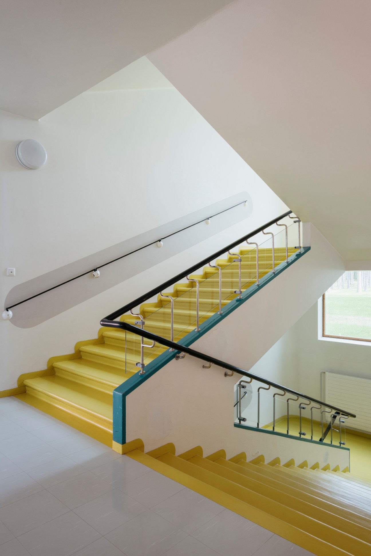 Modernist staircase with yellow-painted steps, white walls, and steel railings at Paimio Sanatorium.