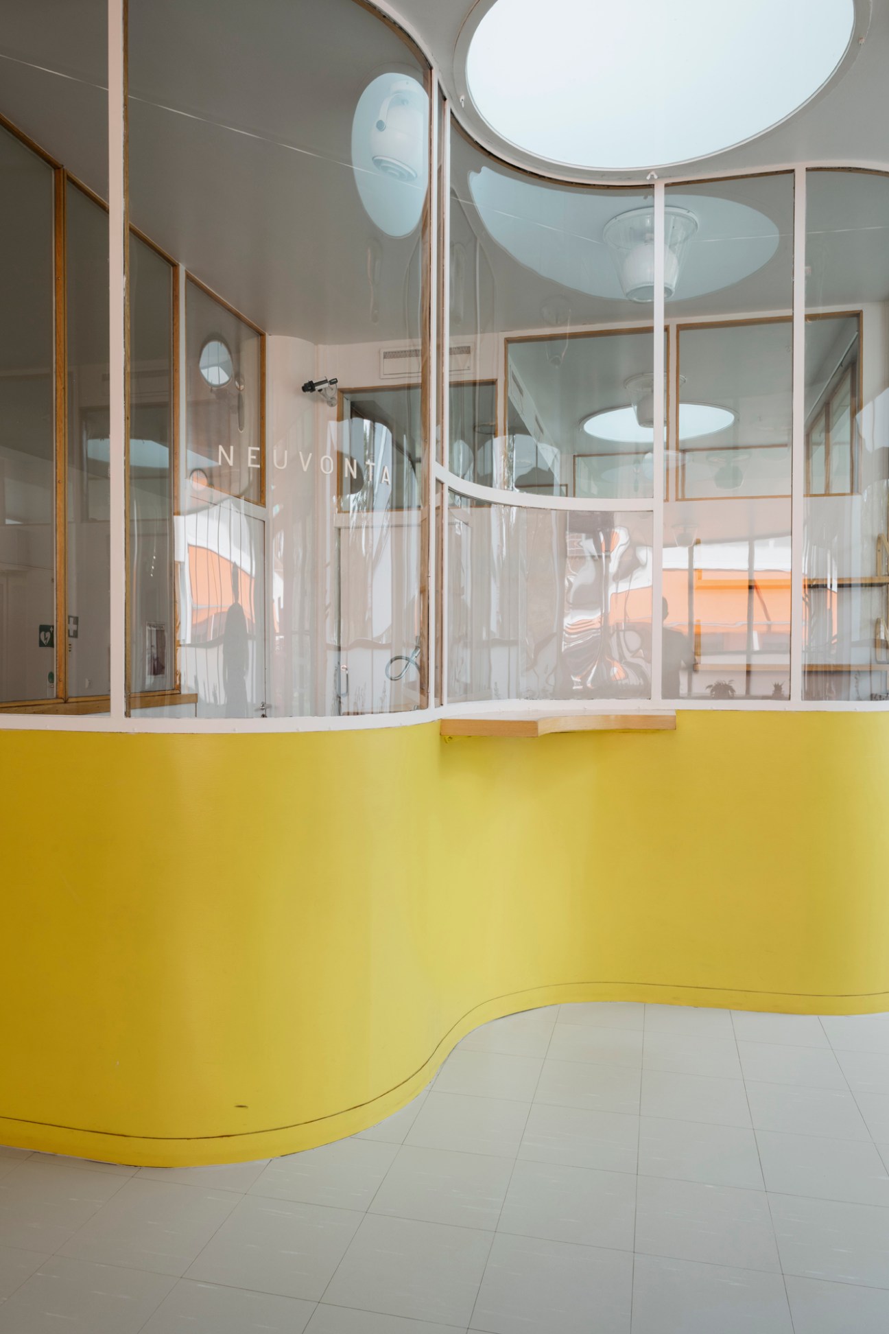 Paimio Sanatorium reception desk featuring curved yellow walls, circular skylights, and glass partitions with bronze frames.