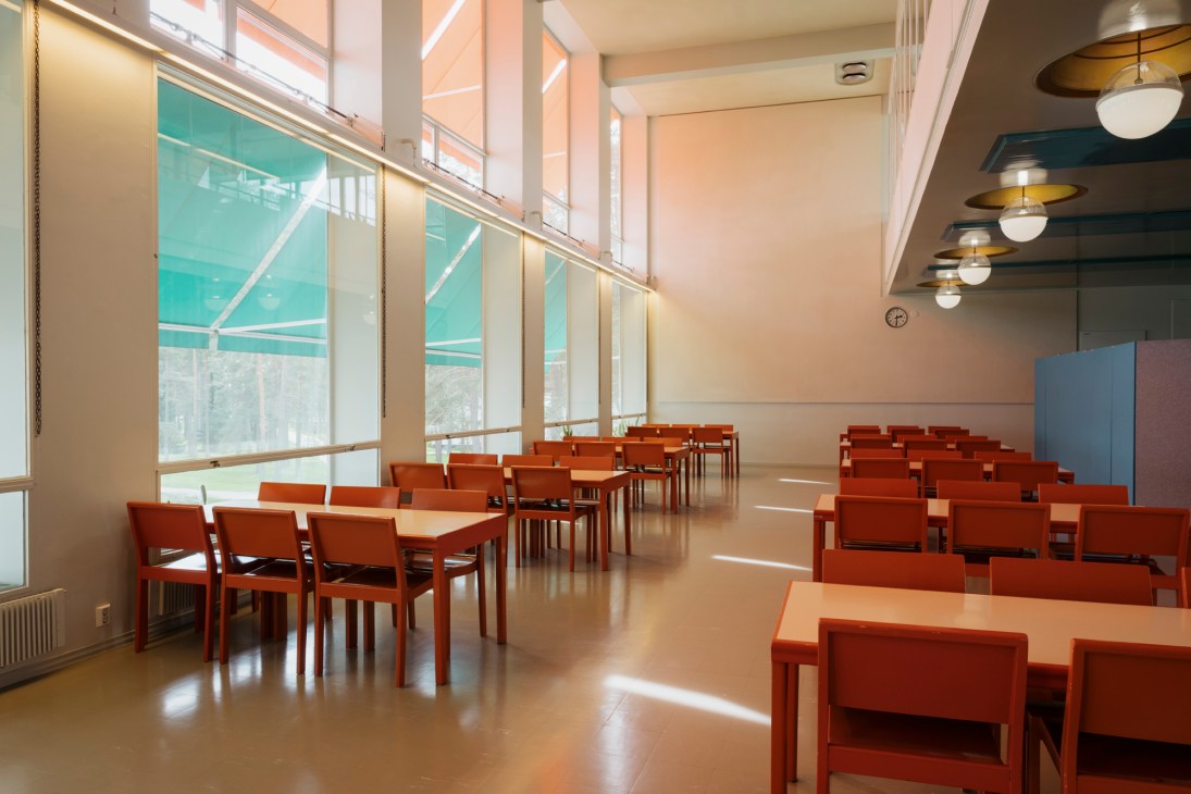 Paimio Sanatorium dining hall with original Aalto furniture, pendant lamps and large windows overlooking forest.