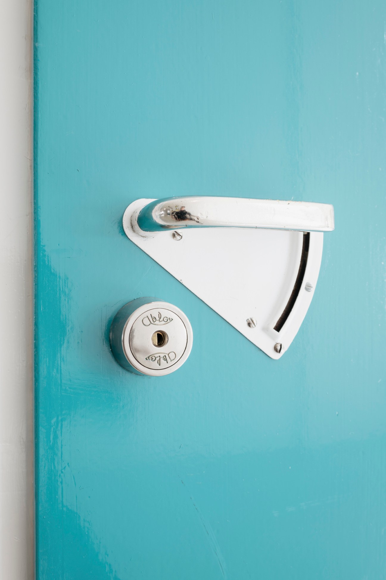 Modernist white door handle and circular lock on a light blue painted wall in a patient's room.