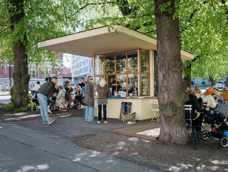 Customers queue at Kiosque, a Helsinki kiosk serving French café classics, with staff taking orders through the window.