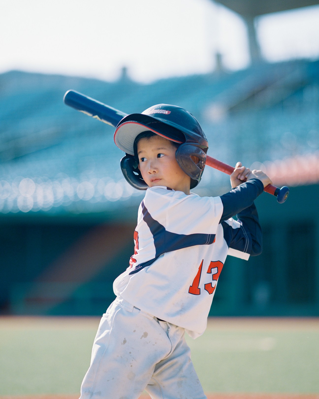 Young baseball player in white uniform with number 13 mid-swing at bat wearing protective helmet