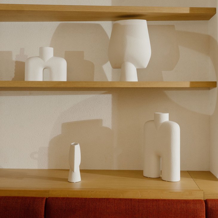 White ceramic vases and vessels displayed on wooden shelves against a textured wall