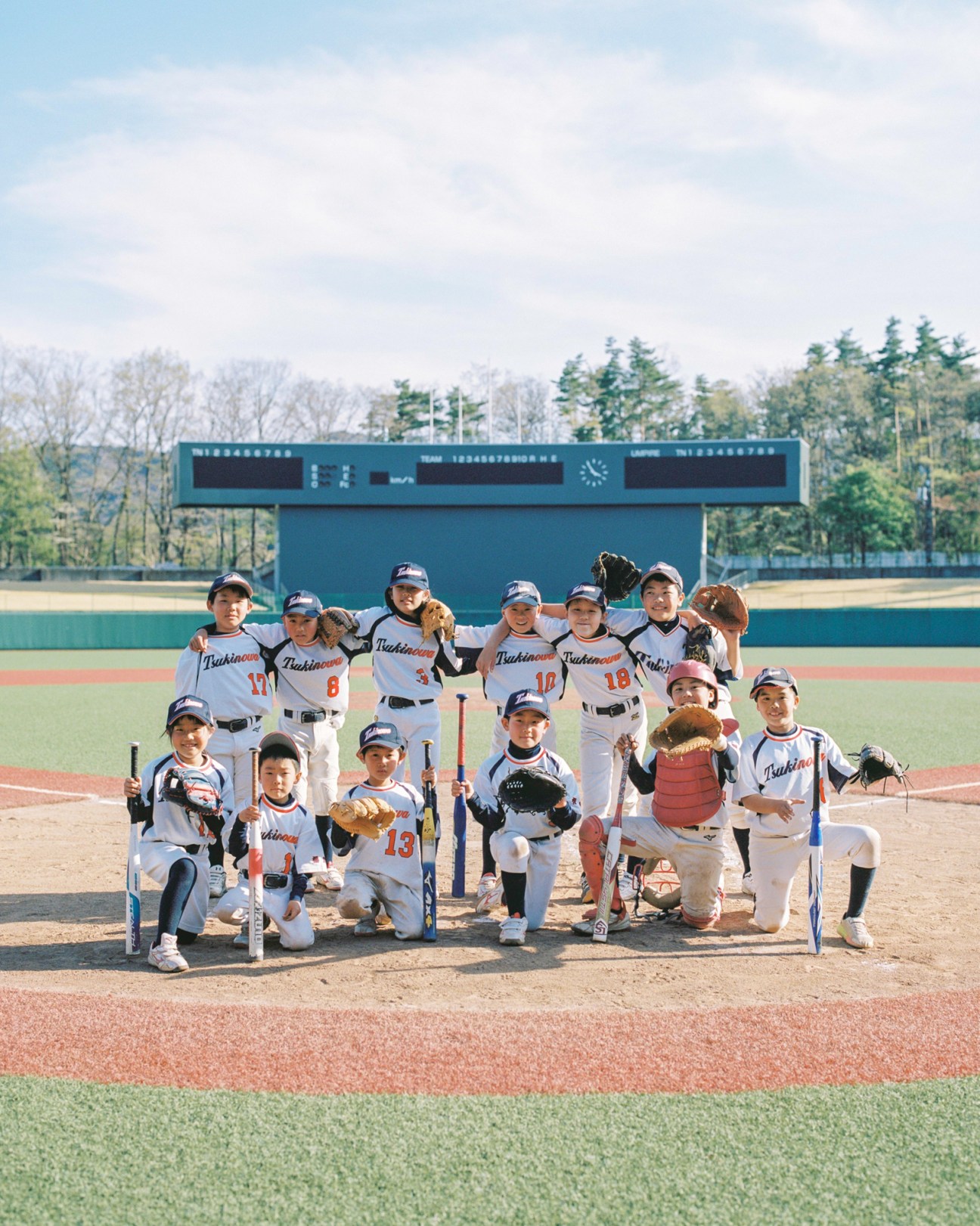 Young softball players from the Tsukinowa Sports Shonendan team posing together at Azuma Baseball Stadium in Fukushima