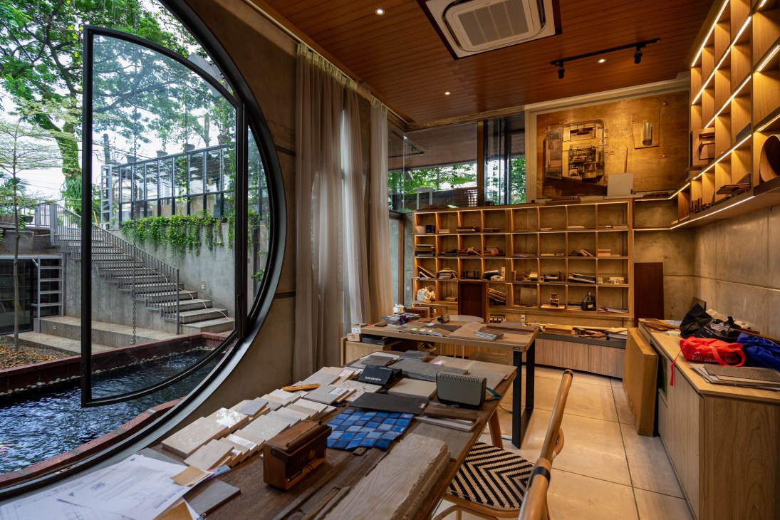 Modern office interior with curved window, wooden shelving, and material samples on low tables