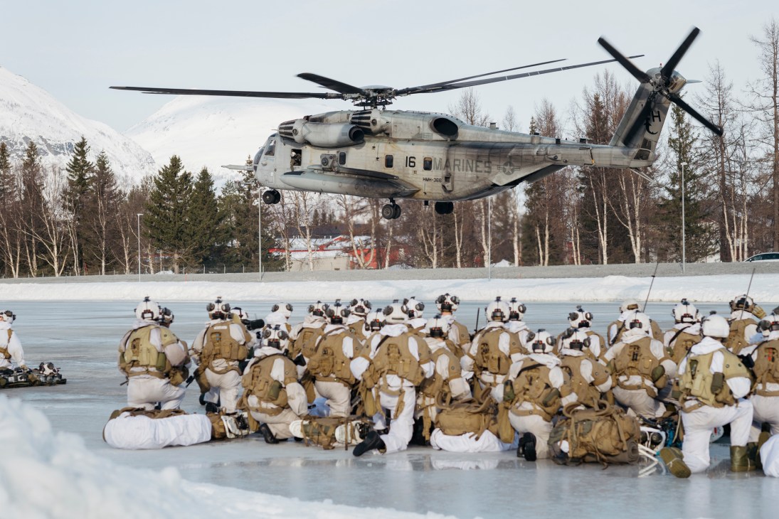 US Marine Corps Super Stallion helicopter hovering above Norwegian conscripts in winter combat gear on snowy ground at Setermoen base.
