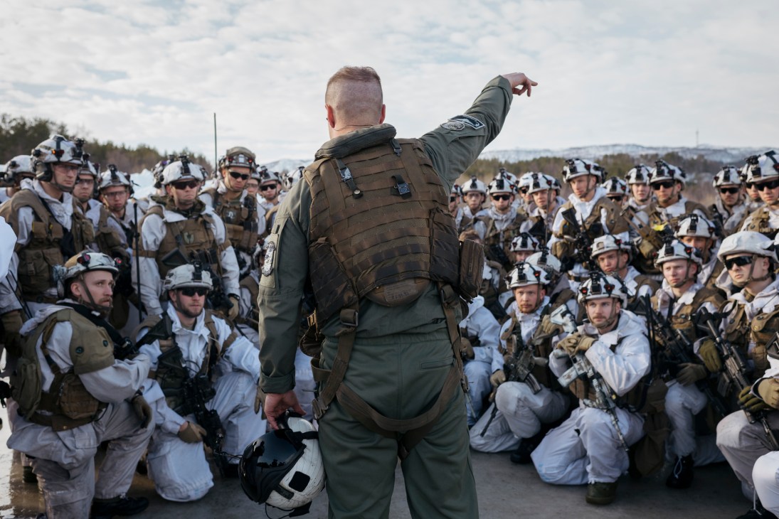US Marine Corps pilot in flight suit briefing Norwegian conscripts standing in formation on snowy ground.