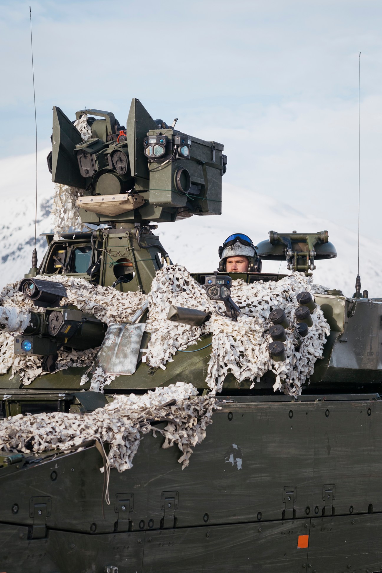 Norwegian army's Swedish-made Hägglunds BV206 all-terrain combat vehicle covered in white camouflage netting in snowy terrain.