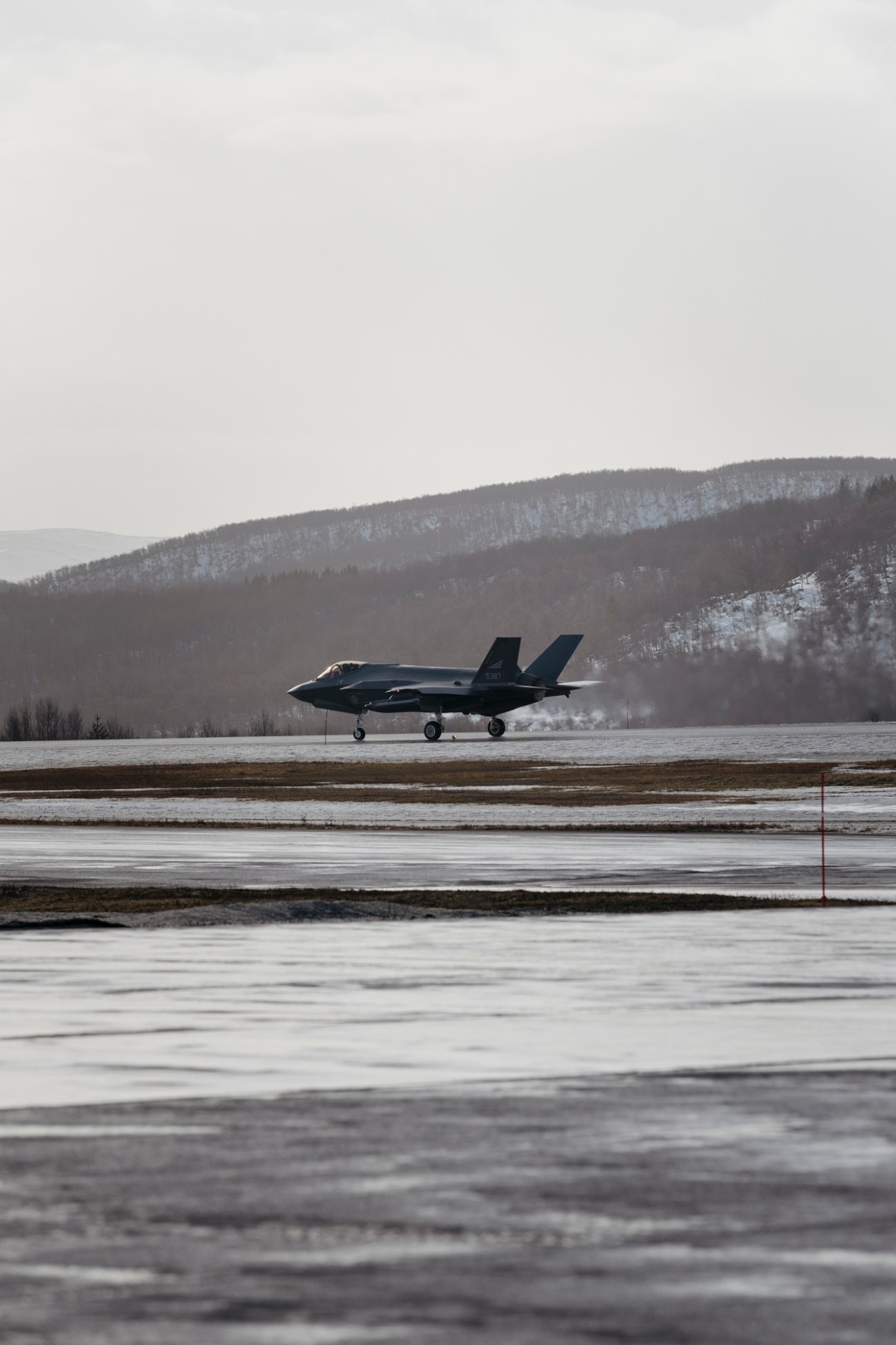 Lockheed Martin F-35 stealth fighter jet parked on a snowy airfield with forested mountains in the background.
