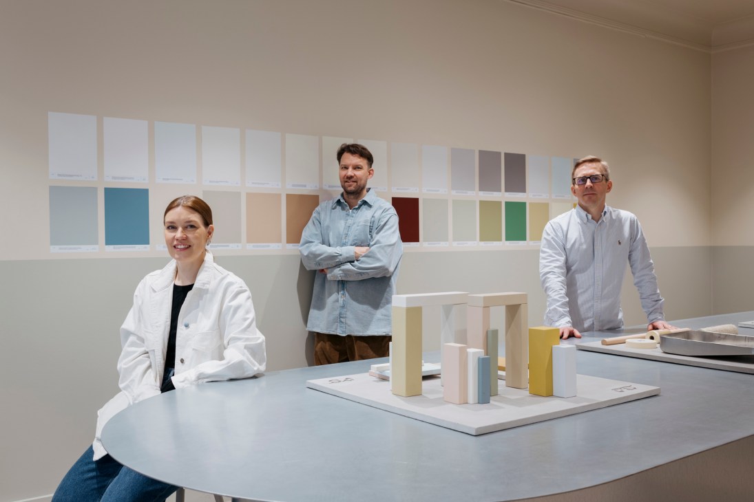 Three people standing in Cover Story Paint shop in Helsinki with colorful paint sample wall display