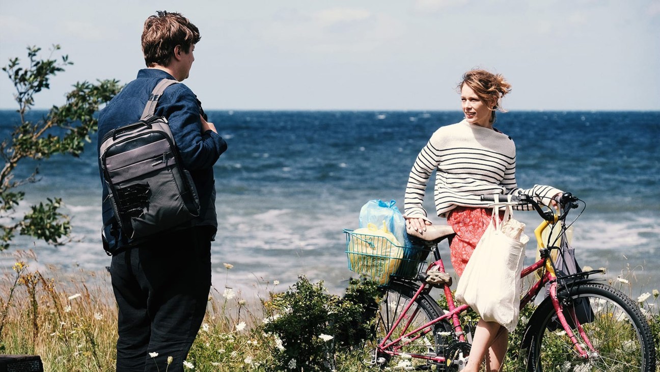 Two people by the seaside with a bicycle and backpack, ocean in background.