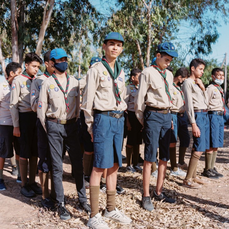 Group of young scouts in uniform with merit badges and neckerchiefs standing at outdoor camp in Tripoli