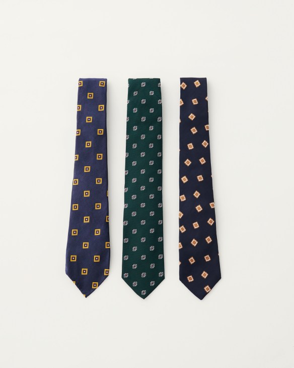 Three neckties displayed vertically with geometric patterns in navy, green, and navy with contrasting square motifs.