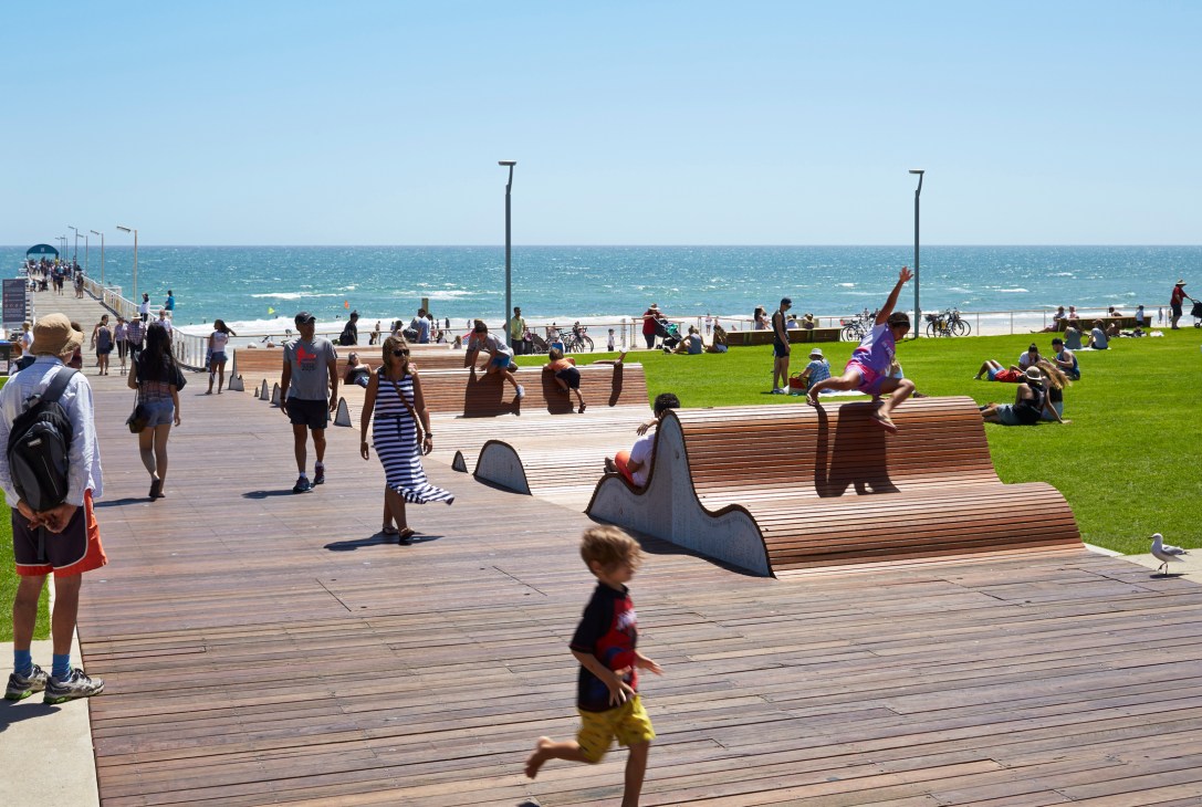 People relaxing on wooden wave-like benches at Henley Square beachfront with ocean and blue sky in background