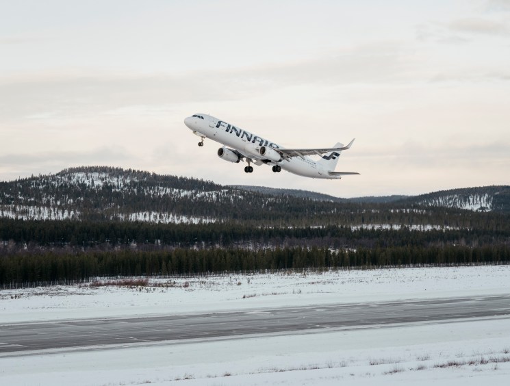 Finnair aircraft taking off from snow-covered runway with forested hills in background at Ivalo Airport